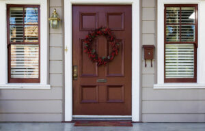 Burgundy front door with wreath and white trimmed windows with blinds on either side